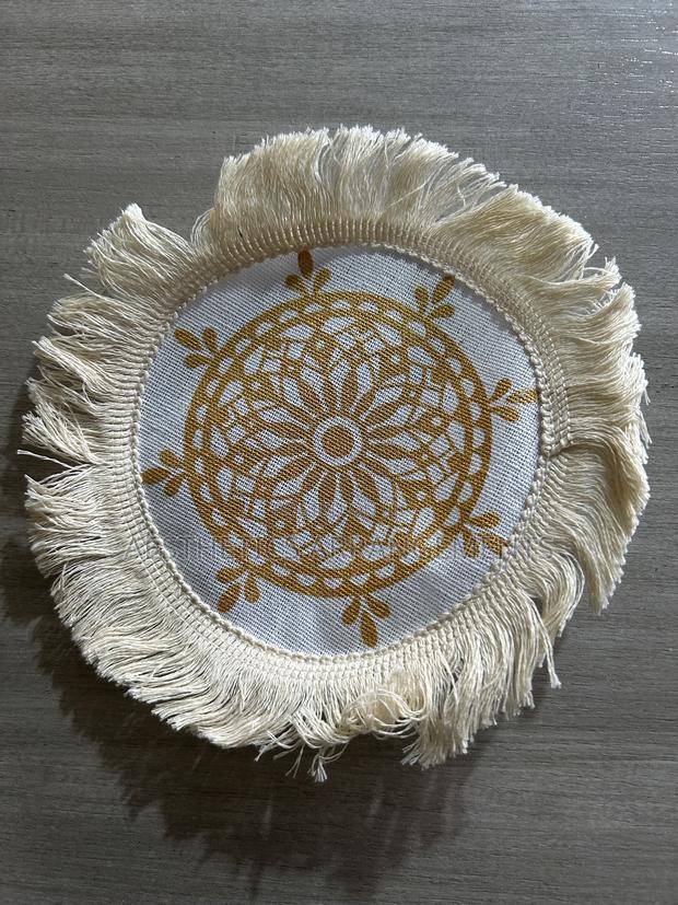 Off-White Coaster With Brown Ship Helm and White Tassels.